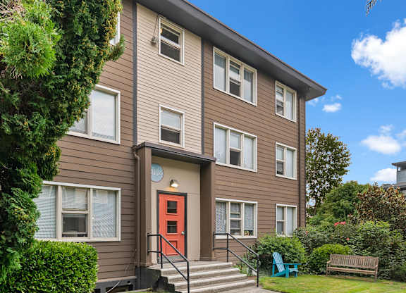 A brown house with a red door and a green chair in front.
