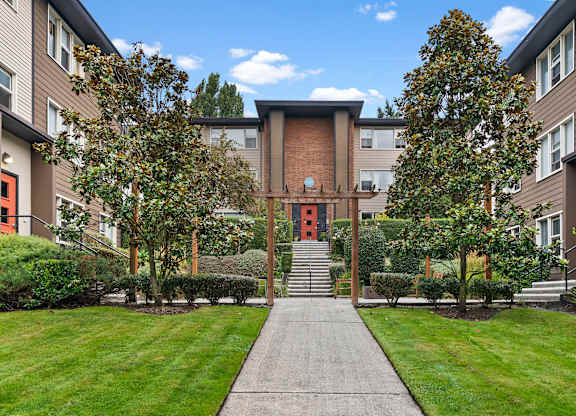 A building with a red door is surrounded by trees and bushes.