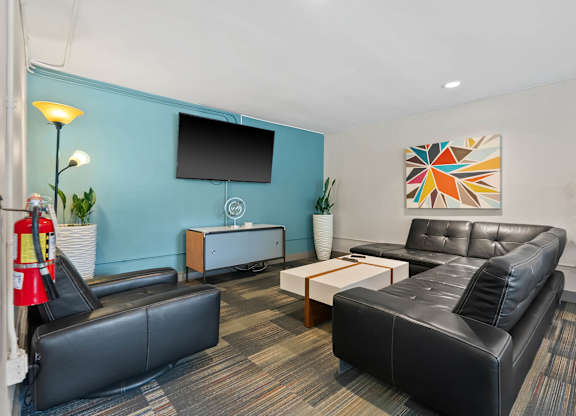 A black leather couch sits in a room with a blue wall and a television.