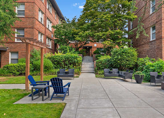 A courtyard with a concrete floor, blue chairs and tables, and a brick building in the background.