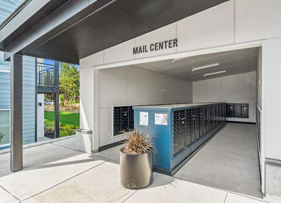 A mail center with a blue mailbox and a plant in a pot.