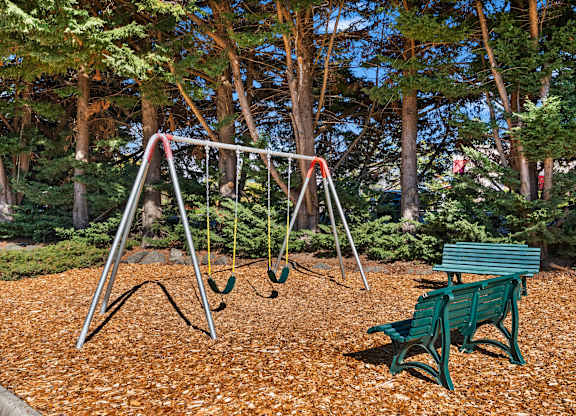 A swing set with a green bench in front of a tree.