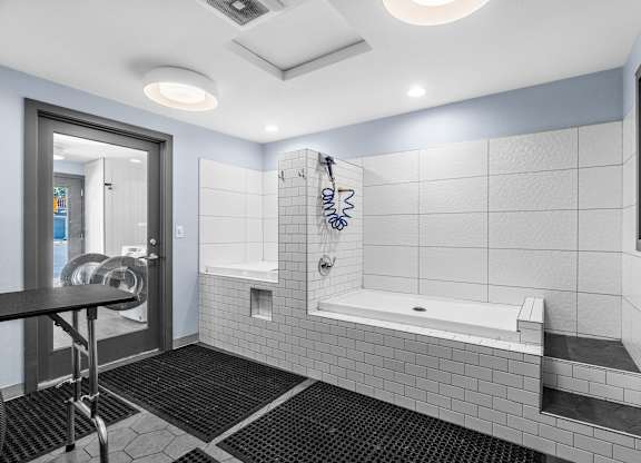 A bathroom with a white tiled shower area and a black mat on the floor.