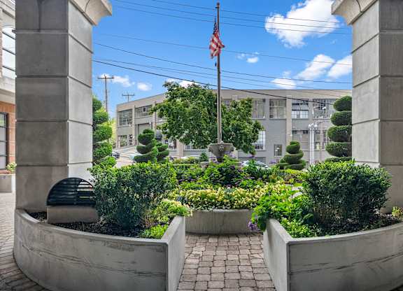 A garden with a flag on a pole is framed by two concrete pillars.