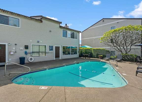 A swimming pool in front of a building with a tree to the right.