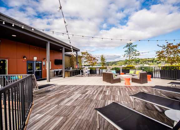 A wooden deck with chairs and tables is surrounded by a black railing. at The Platform, Kent, 98032