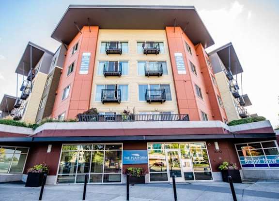 A multi-story building with a red and beige facade and balconies on the upper floors. at The Platform, Kent, 98032