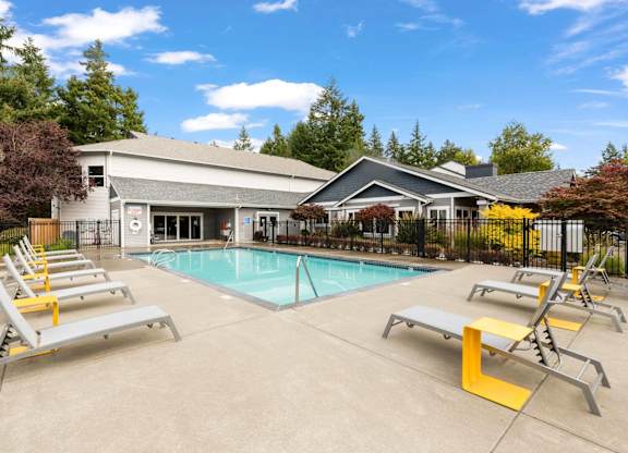 A pool with sun loungers and a building in the background.