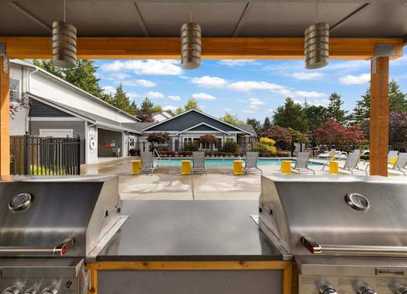 A grill is in the foreground of a backyard with a pool and a house in the background.