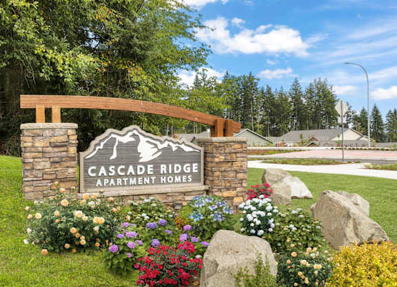 A sign for Cascade Ridge Apartment Homes is surrounded by flowers and rocks.