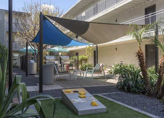 A patio with a blue shade sail and a concrete table with yellow bowls on it.