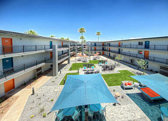 A sunny day at the courtyard of a building with blue umbrellas and orange doors.