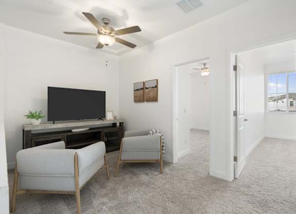 A living room with a television, two chairs, and a ceiling fan.
