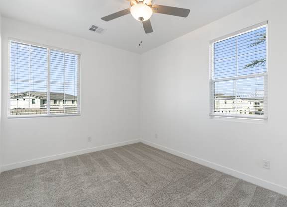 A room with a ceiling fan and two windows.