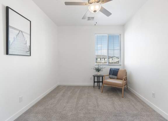 A room with a ceiling fan, a chair, and a small table with a plant on it.