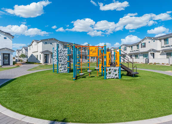 A playground with a slide and climbing wall in front of apartment buildings.
