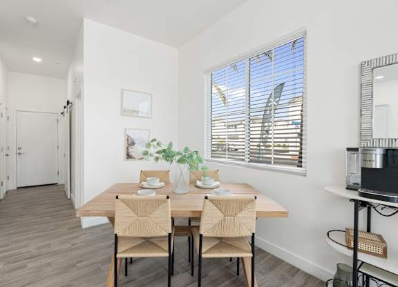 A dining room with a table set for two and a potted plant on the windowsill.