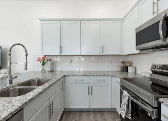 A kitchen with white cabinets and a black microwave.