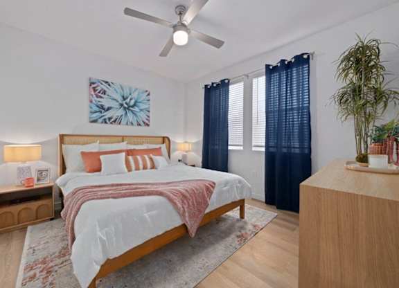A bedroom with a large bed, a ceiling fan, and a potted plant.