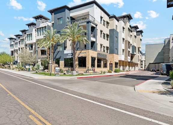 A street view of a residential area with modern buildings and palm trees.