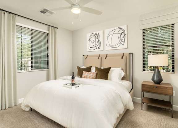 A bedroom with a large bed, a nightstand with a lamp, and two abstract art pieces on the wall.