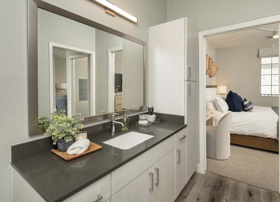 A bathroom with a vanity, mirror, and a bed in the background.