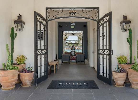 A black gate with a metal design leads to a hallway with a black mat on the floor that says "SPRING".