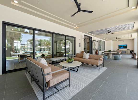 A modern living room with a glass wall and a ceiling fan.