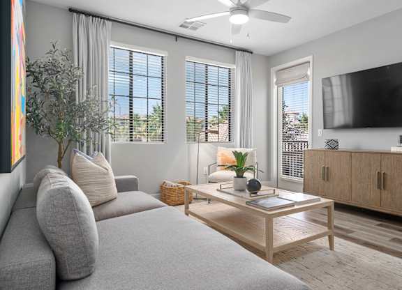 A living room with a grey couch, a wooden coffee table, and a flat screen TV mounted on the wall.