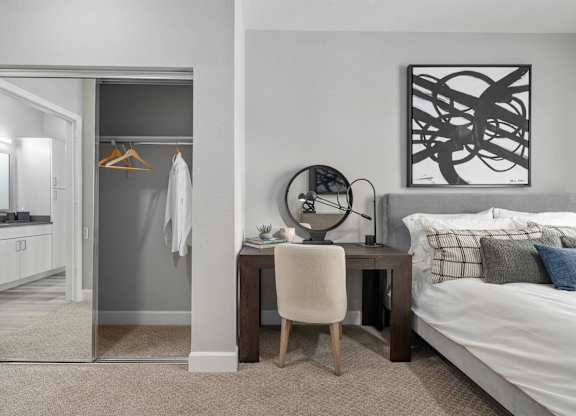 A bedroom with a bed, desk, chair, and a mirror.