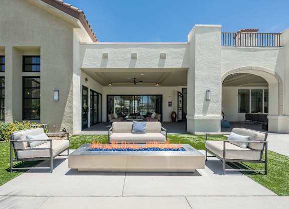 A modern house with a white exterior and a patio with two chairs and a fire pit.