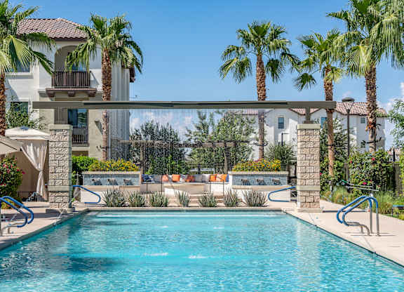 A swimming pool surrounded by palm trees and a white house in the background.