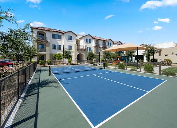 A tennis court is surrounded by apartment buildings.