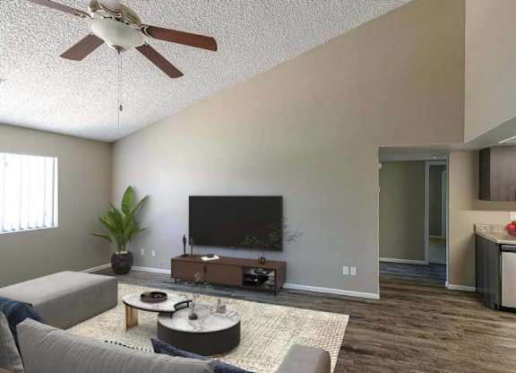 A living room with a grey couch, a coffee table, a television, and a kitchen area in the background.