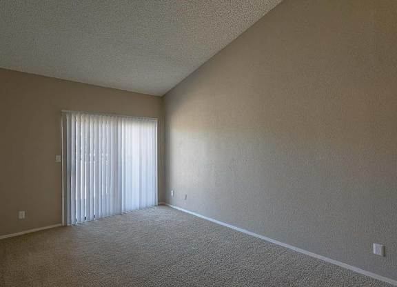 A room with a carpeted floor and a window with blinds.