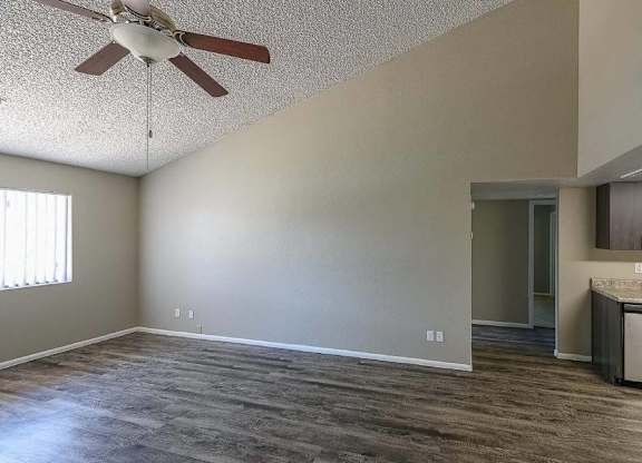A room with a ceiling fan and a kitchen area in the background.