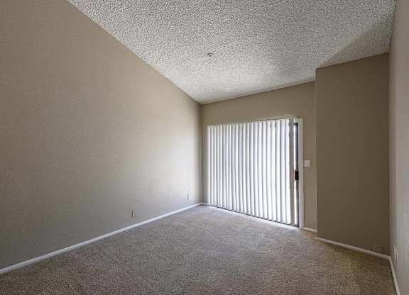 A room with a carpeted floor and a door with vertical blinds.