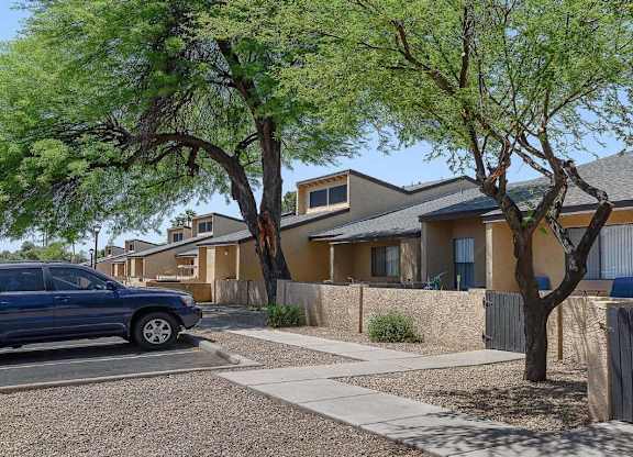 A blue car is parked on the street in front of a house with a tree in front of it.