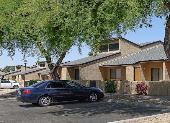 A blue car is parked in front of a house with a tree in front of it.