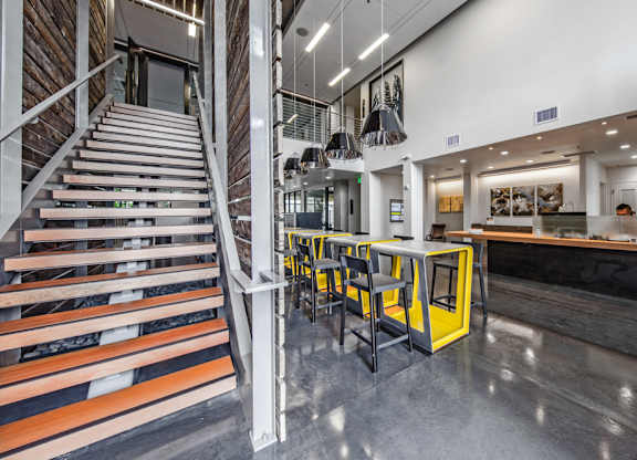 A staircase with wooden steps and metal railings leads to a brightly lit room with a bar and seating area.