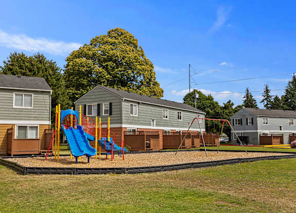 A playground with a blue slide and a red swing set in front of a row of houses.
