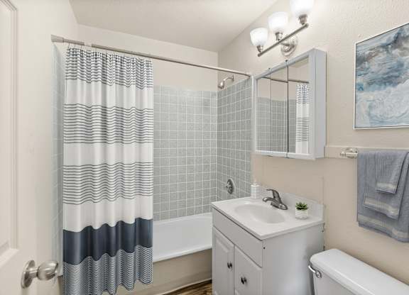 A bathroom with a white sink, a white toilet, a white bathtub, a white cabinet, a white shower curtain, a white tiled wall, a white door, a white light fixture, a white to