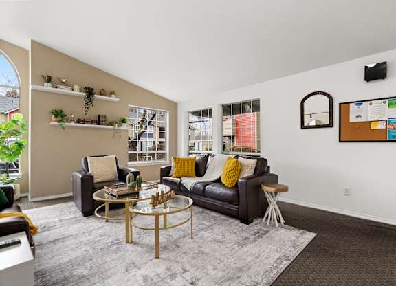 A living room with a black couch, a coffee table, and a wall with a bulletin board and a plant.
