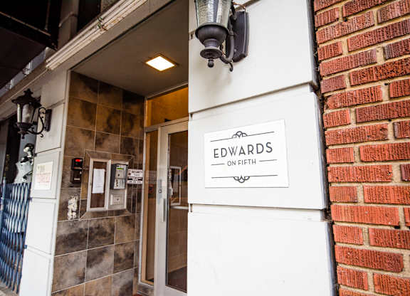 The entrance to Edwards on Fifth is shown with a brick wall on the right and a metal gate on the left.