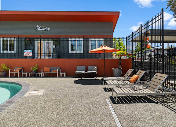 A pool area with a red building and lounge chairs.