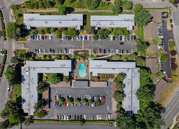 An aerial view of a parking lot with cars and a building with a pool in the middle.