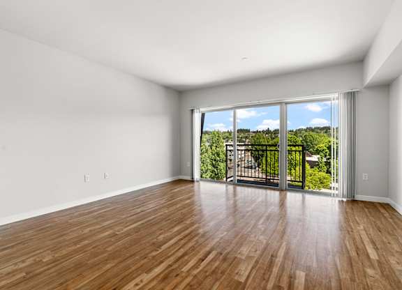 A room with wooden floors and a sliding glass door leading to a balcony.