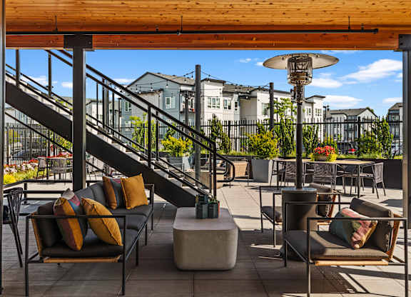 A patio with a black couch and a table with a lamp on it.