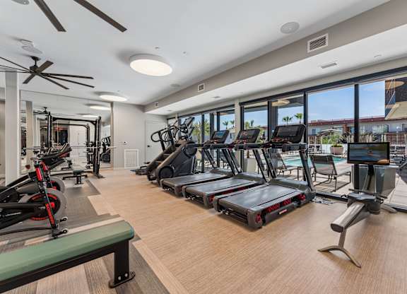 A gym with treadmills, exercise bikes, and a fan.