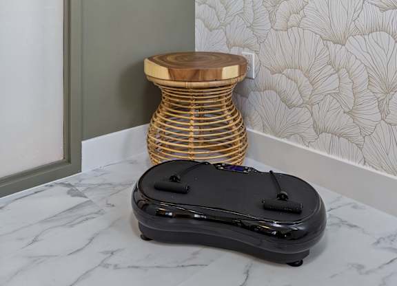 A black suitcase sits on a marble floor next to a round wooden stool.